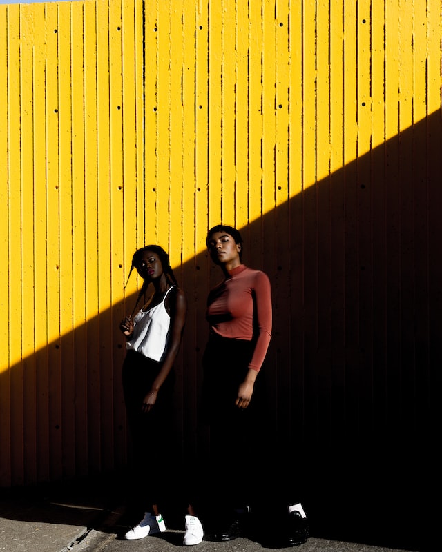 Two young black women next to a wall